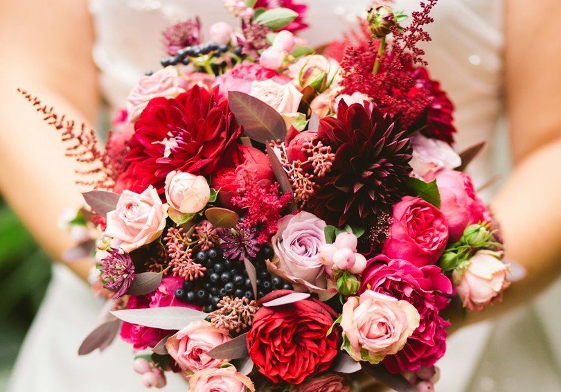 A bouquet of flowers held by a bride, featuring shades of pink from pale to burgundy.