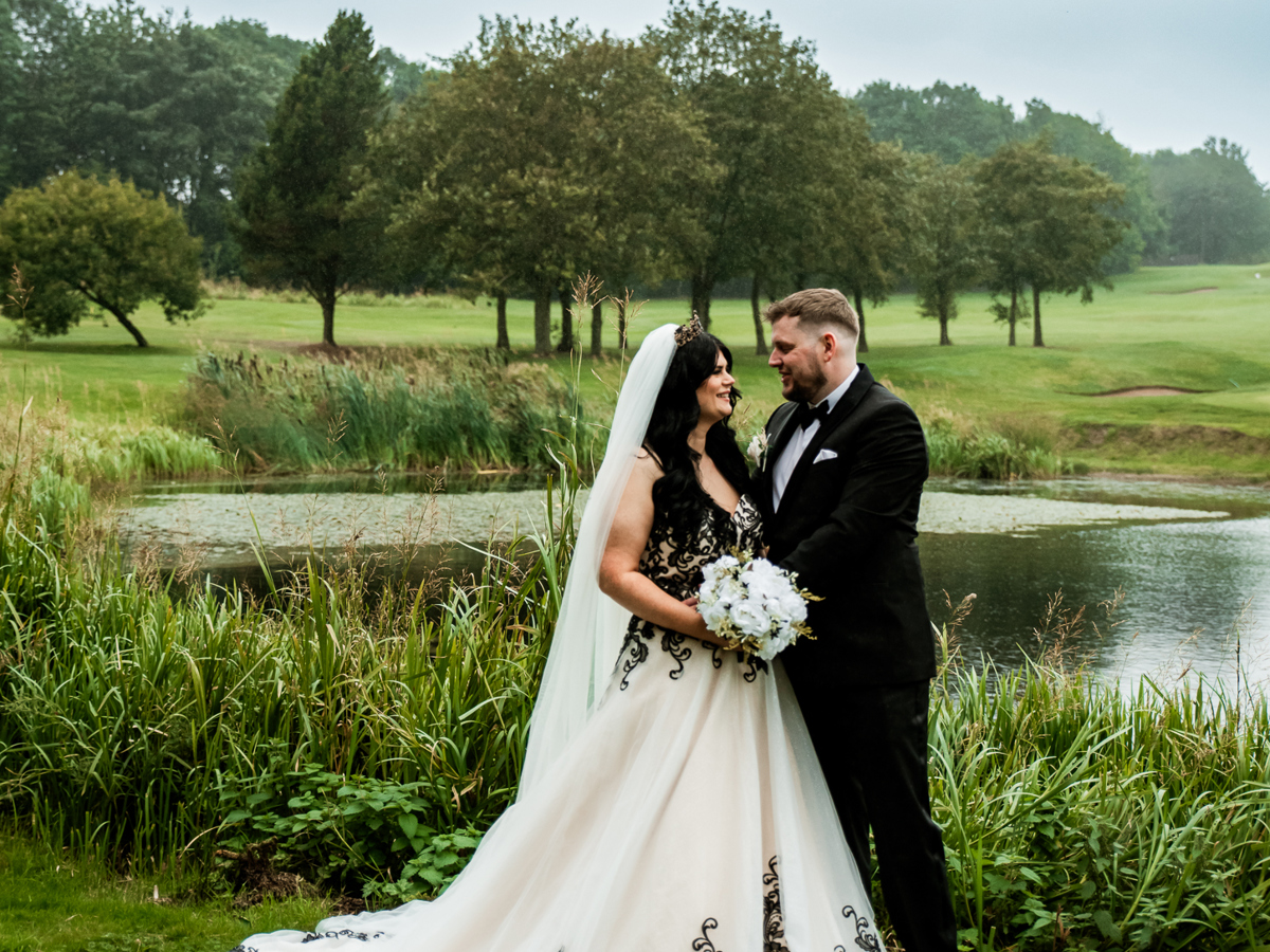 A bride and groom embrace beside The Lake at The Manor Leeds.