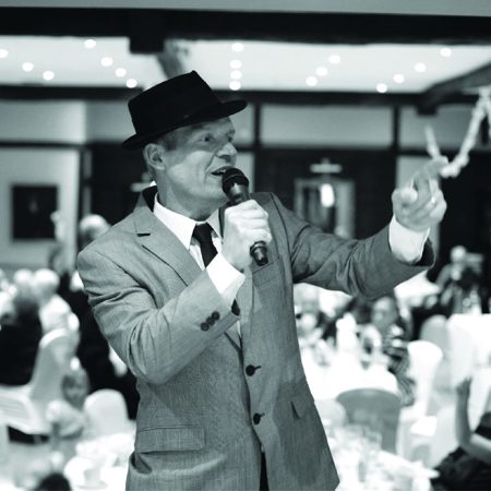 A black and white photo of Frank Sinatra tribute Phil Fryer singing into a microphone.