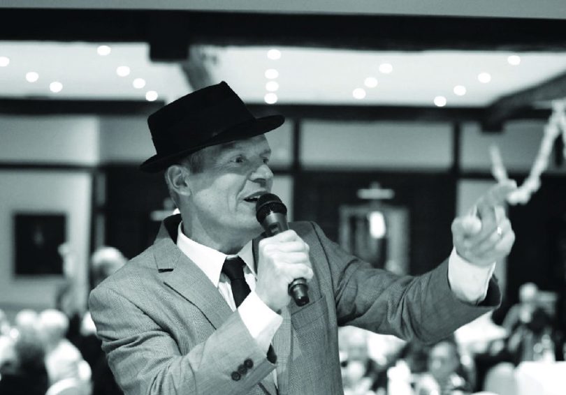 A black and white photo of Frank Sinatra tribute Phil Fryer singing into a microphone.