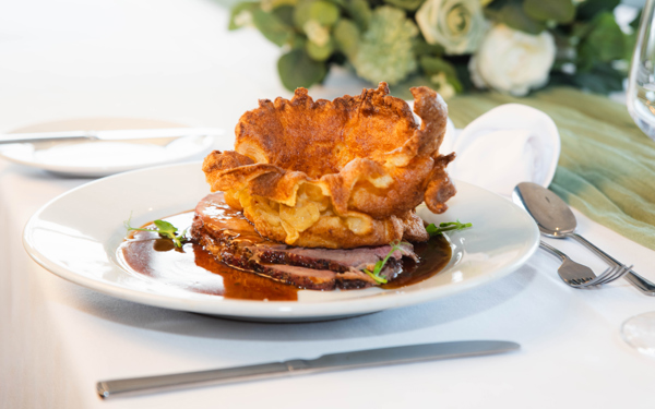 Roast beef on a plate, with Yorkshire Pudding and gravy placed on a formal dining table.