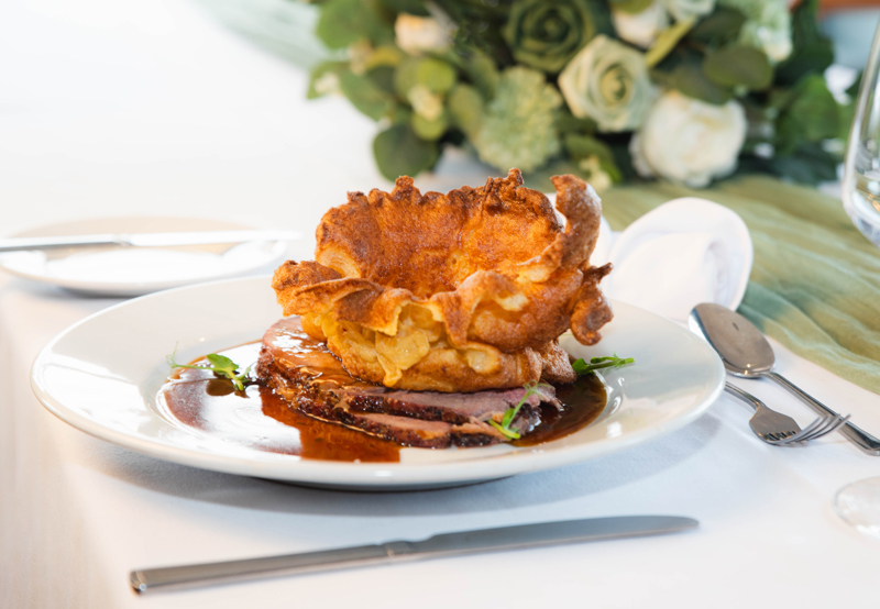 Roast beef on a plate, with Yorkshire Pudding and gravy placed on a formal dining table.