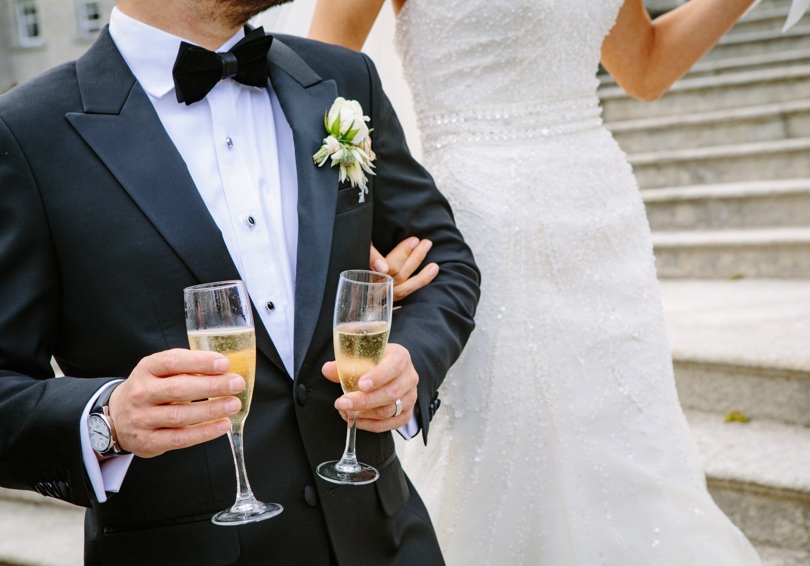 A headless shot of a bride and groom, the groom is holding two flutes of champagne.