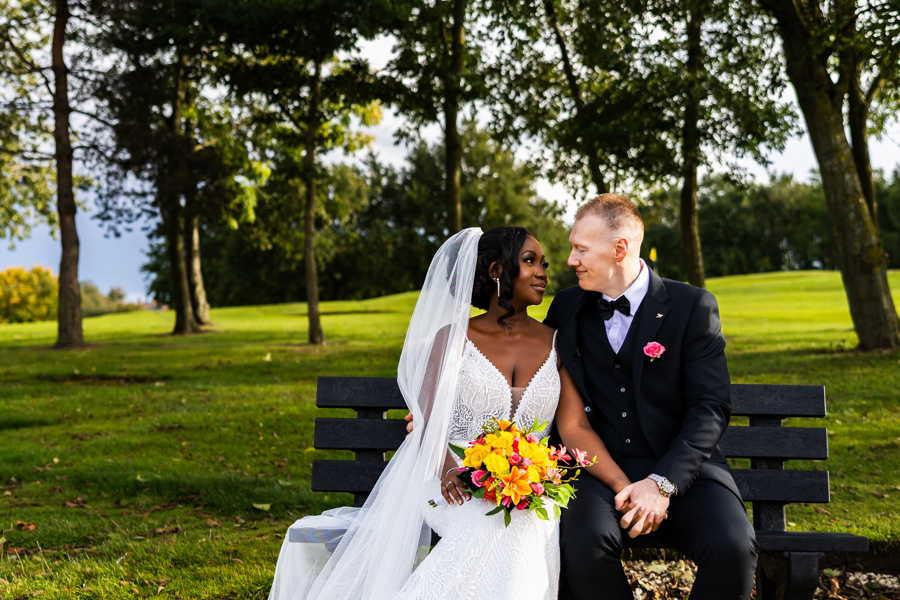 A bride and groom gaze at each other while sitting on a bench at The Manor Leeds.