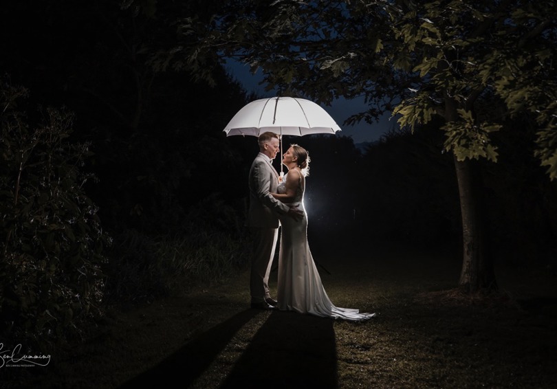 A night shot of bride and groom embracing under a white umbrella.