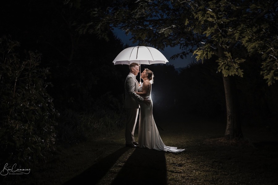 A night shot of bride and groom embracing under a white umbrella.