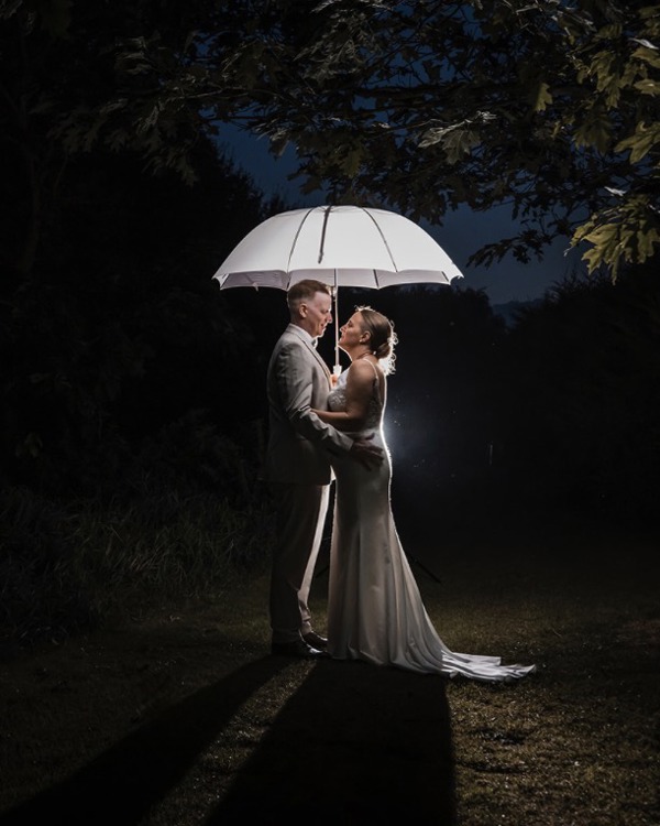 A night shot of bride and groom embracing under a white umbrella.