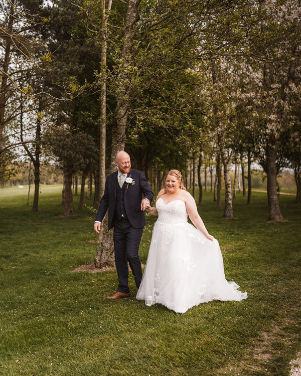 A bride and groom walk hand-in-hand through trees at The Manor Leeds.