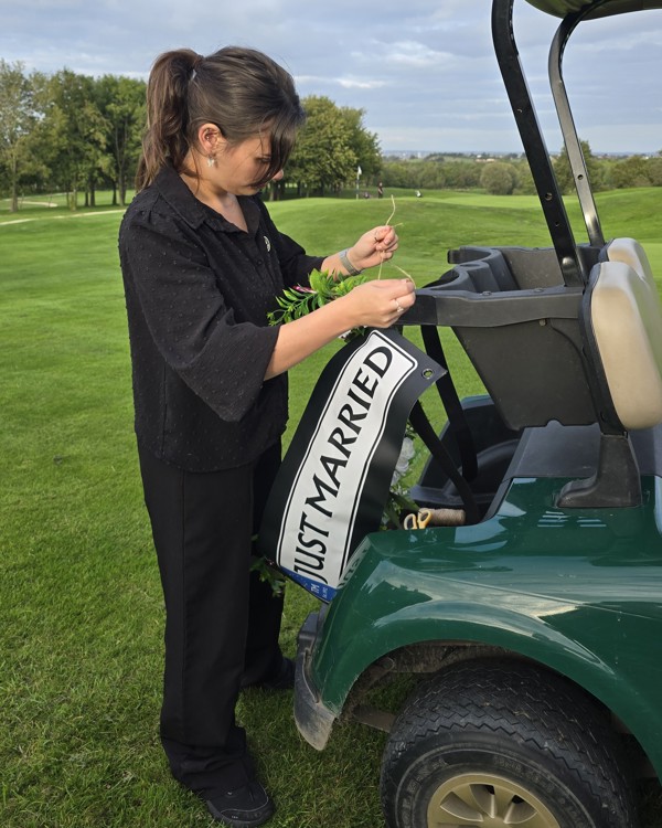 The Manor Assistant Events Manager Starr fastening the "Just Married" sign to a golf buggy.