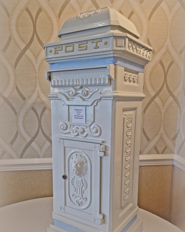 A vintage white postbox decorated with pale blue ribbon.