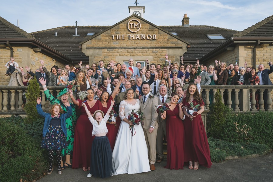 A bride and groom with their guests at the front of The Manor building.