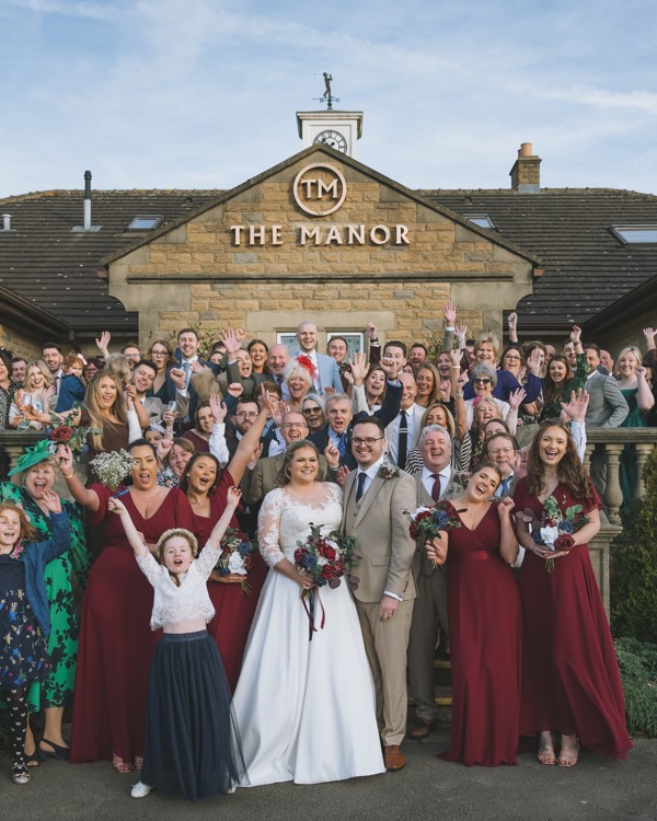 A bride and groom with their guests at the front of The Manor building.