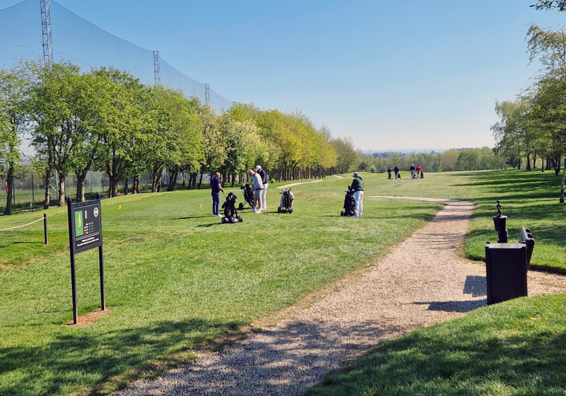 A view of the first tee at The Manor golf course, four male golfers are standing at the tee and four are walking away along the fairway.