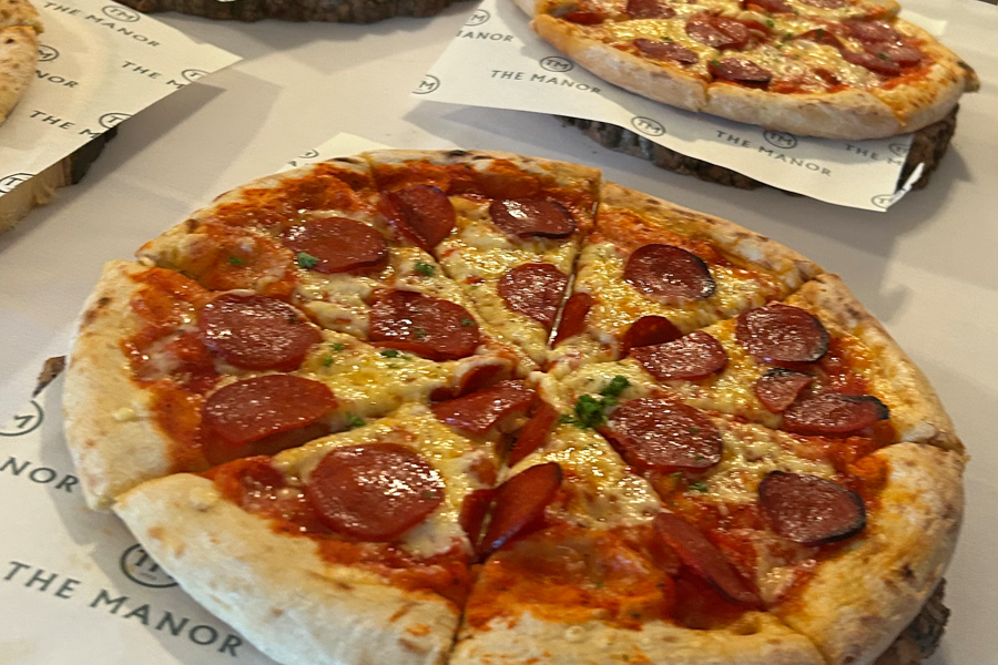 Pepperoni pizza presented on greaseproof paper printed with The Manor logo on a buffet table at The Manor Leeds.