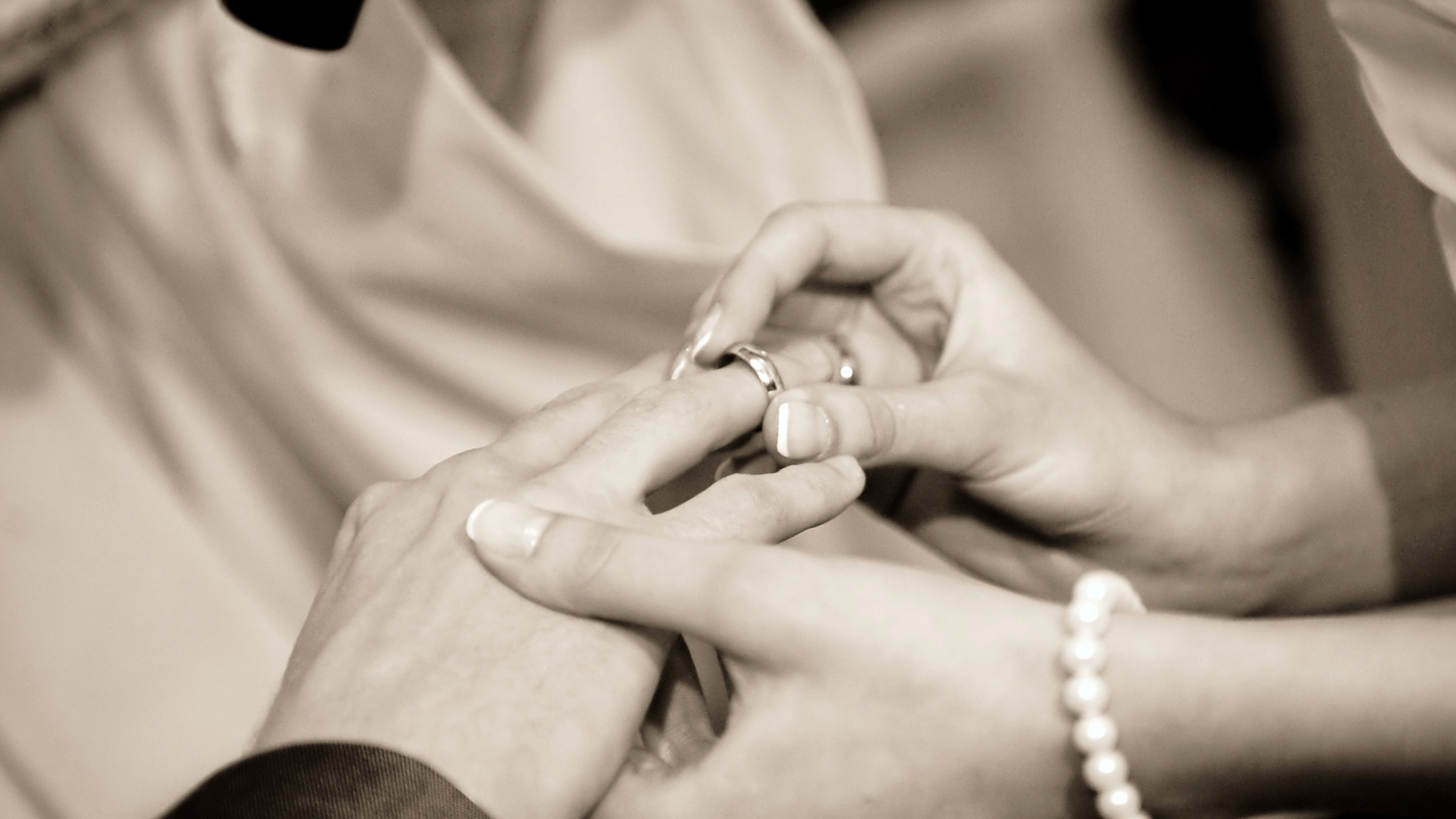 A sepia photo of a female hand placing a wedding ring on a male hand.