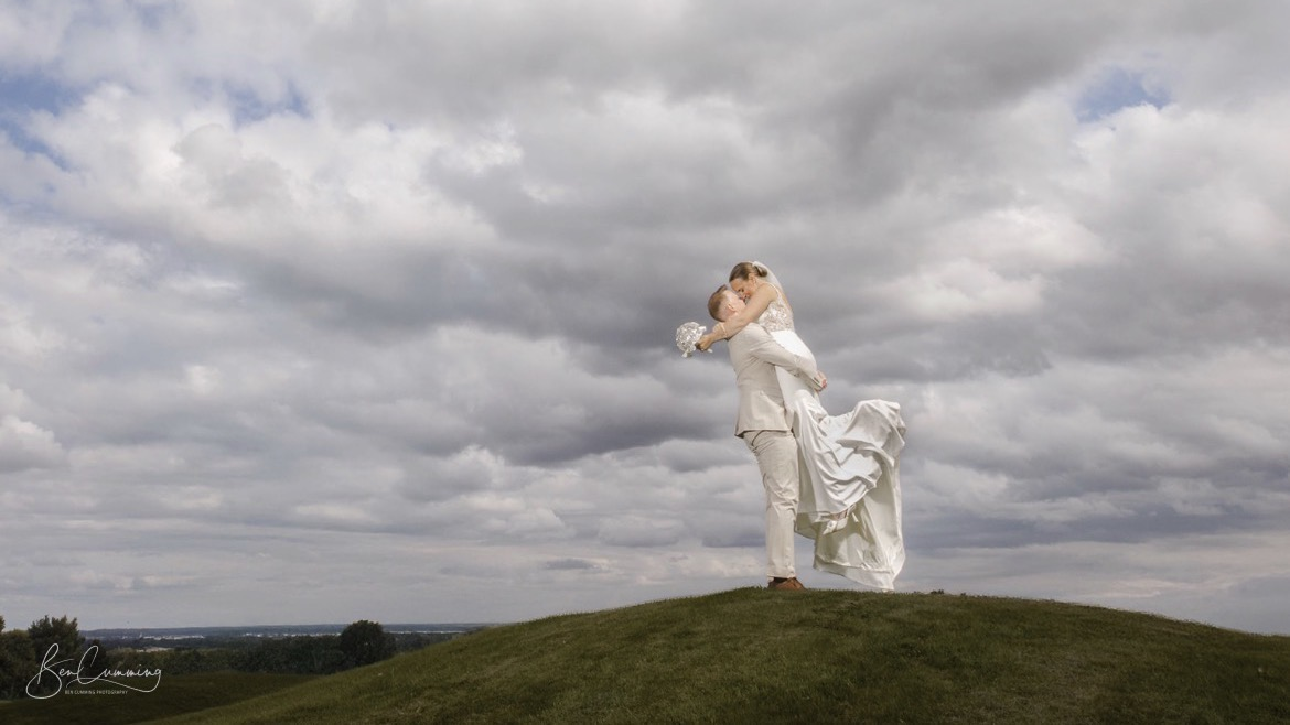 A groom lifts his bride beneath a moody sky at The Manor Leeds.