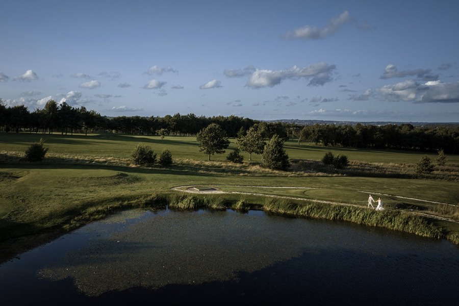 An aerial shit of a bride and groom walking hand-in-hand by The Lake at The Manor Leeds.
