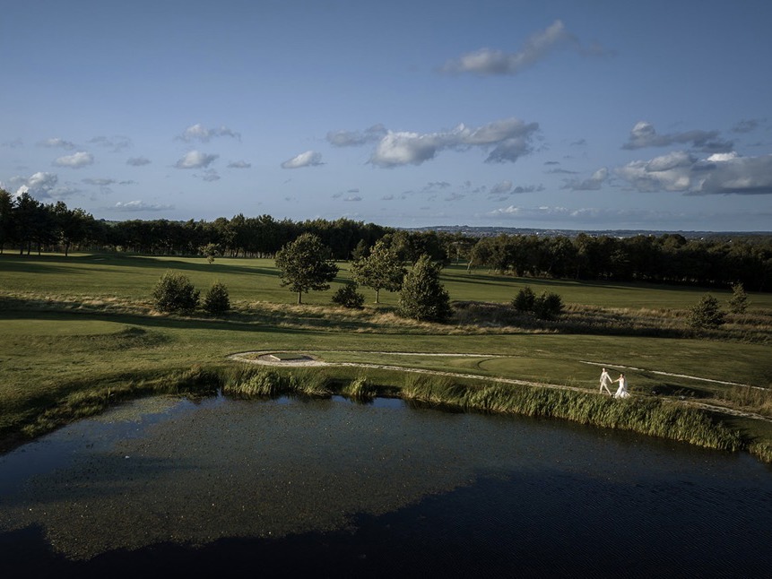 An aerial shit of a bride and groom walking hand-in-hand by The Lake at The Manor Leeds.