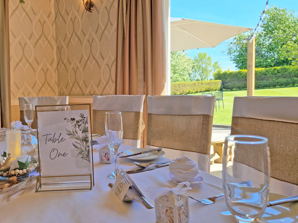 A view over a table set for a wedding breakfast in the High Garden room at The Manor, looking out of the open doors towards The Lawn and patio.