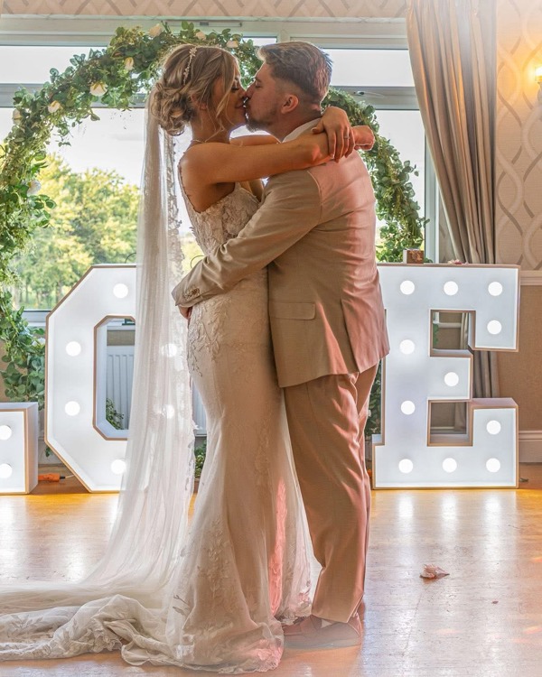 A bride and groom embrace on The Manor's dancefloor in front of a floral hoop and large light-up letters spelling the word "LOVE".
