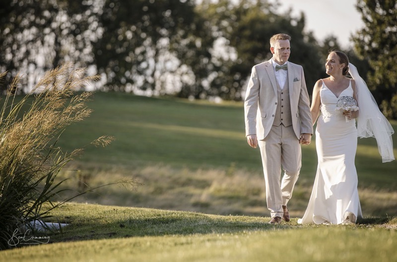 A bride and groom walk hand-in-hand by The Lake at The Manor Leeds.