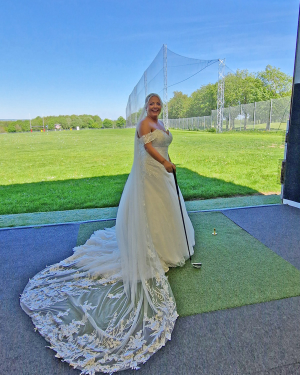 A bride smiles in The Manor's driving range holding a golf club.