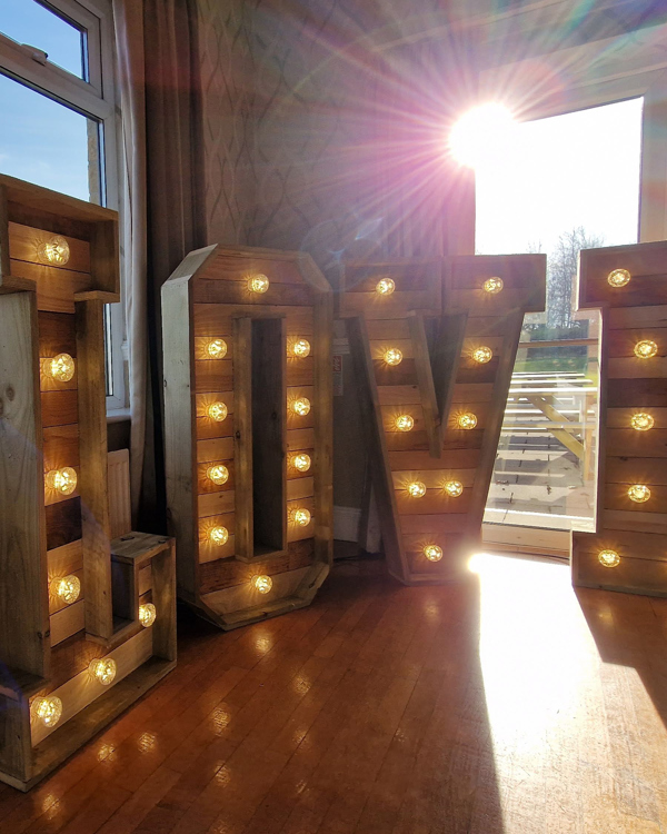 Large, rustic wooden light-up letters spelling the word "LOVE" in the corner of the dancefloor at The Manor Leeds.