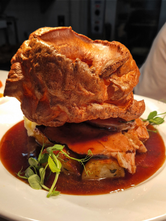 Roast dinner on a plate, Yorkshire Pudding, beef, roast potatoes and gravy.