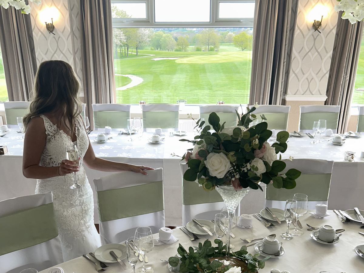 A bride looking out at the view over The Manor golf course, standing beside a table set for a wedding breakfast.
