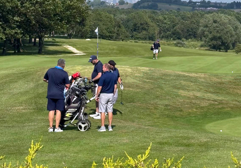 A group of four golfers standing beside the 18th green at The Manor Leeds.