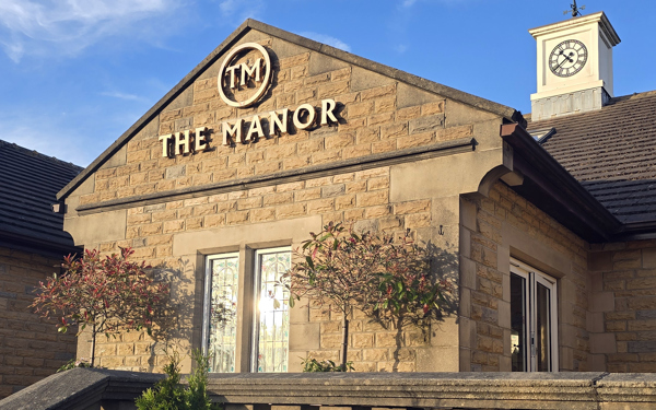 The main entrance of The Manor, showing the stone balustrade, the clocktower and the gold logo.