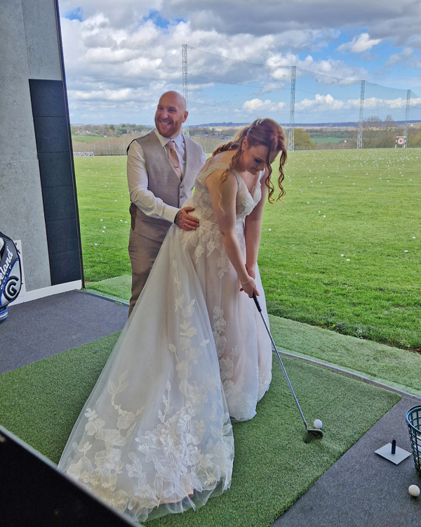 A bride takes a shot in The Manor's driving range, her groom stands behind her, his hands on her hips.