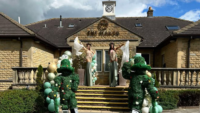 Stilt walkers pose by the main entrance of The Manor Leeds.